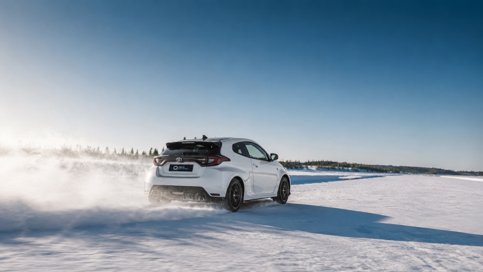 GR Yaris carving through snow spray under a clear blue sky